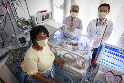 Two doctors and a mother pose in PICU with baby in care.