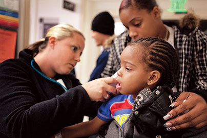 Nurse checkes temp. of young boy while sitting next to his father