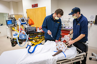 Two transport staff practice on medical dummy on gurney, using oxygen mask and injecting fluid