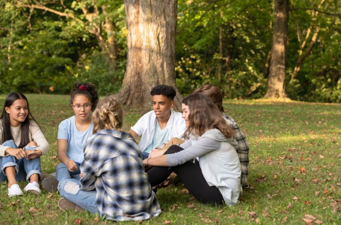 A group of teens sitting in the grass and chatting