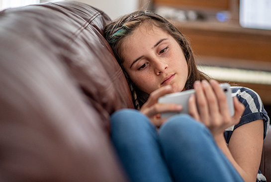 Teen laying on couch staring at phone