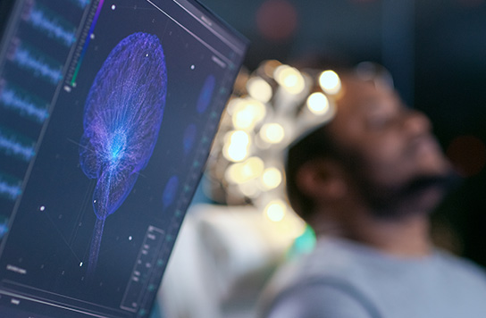 person laying in bed with electrodes attached and computer in foreground showing brain image