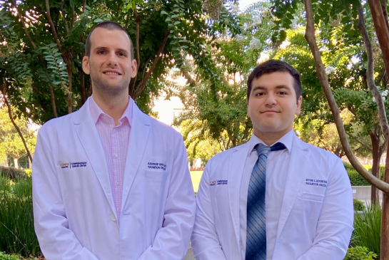 Two medical physics residents wearing white coats standing and smiling outdoors