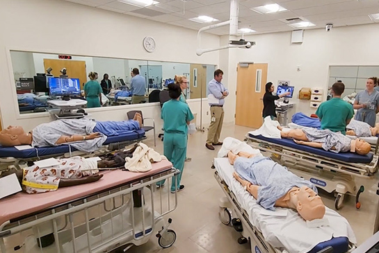 A class working in a simulation room with equipment and mannequins.