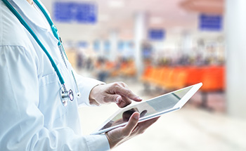 person with white coat and stethescope looking at an Ipad