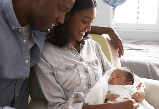 This is a stock photograph of a couple happily cradling their newborn baby, in a hospital setting